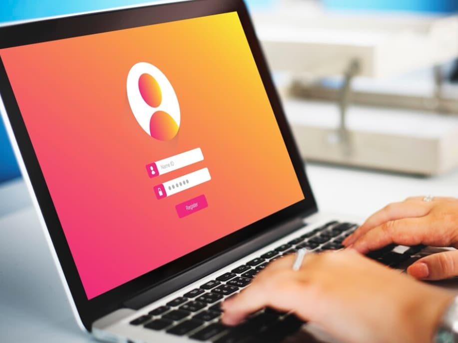 A person's hands typing on a laptop with a colorful login screen displayed